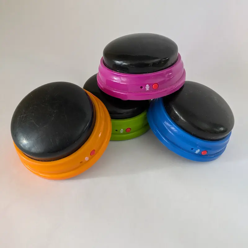 Une pile de boutons de communication colorés et enregistrables pour chiens en orange, violet, vert et bleu.
