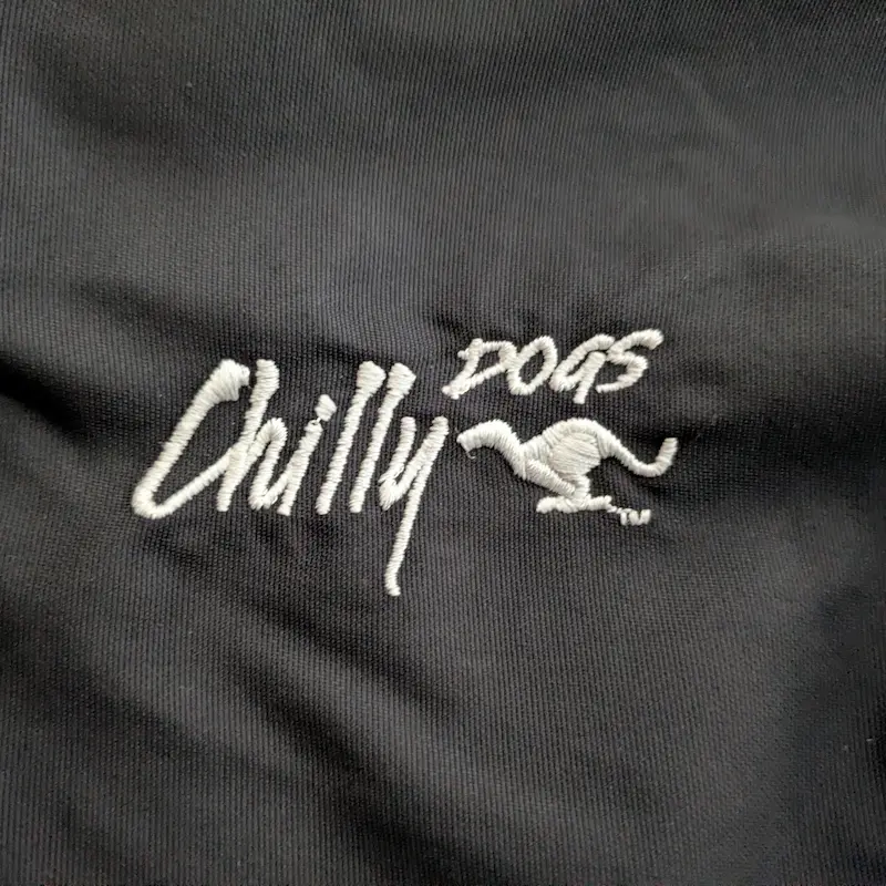 Close-up of the "Chilly Dogs" embroidered logo on the black winter coat fabric.