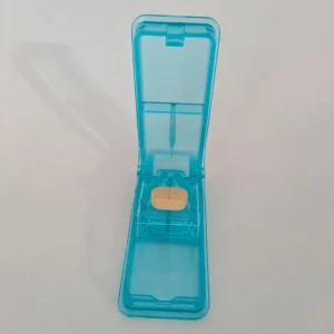 Un diviseur-pilule bleu ouvert avec un comprimé beige positionné dans le support en V prêt à être coupé.