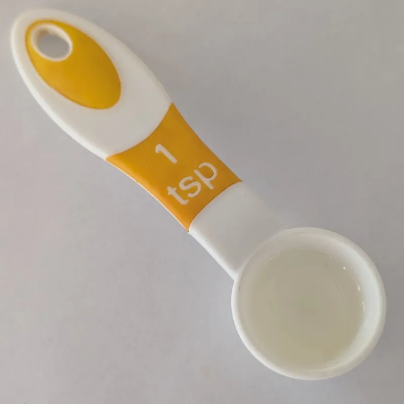 Une cuillère à mesurer en plastique blanc et jaune utilisée pour administrer l'huile de loup marin.