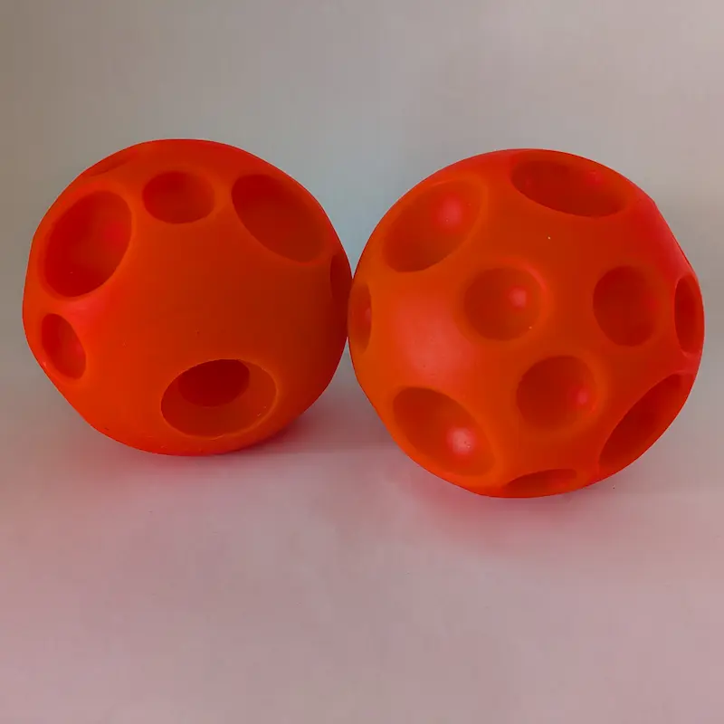 Close-up of two orange interactive dog balls showing the holes for treats.