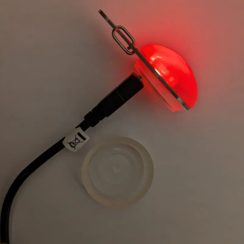 Close-up of a Nite Ize LED collar light glowing red during charging.