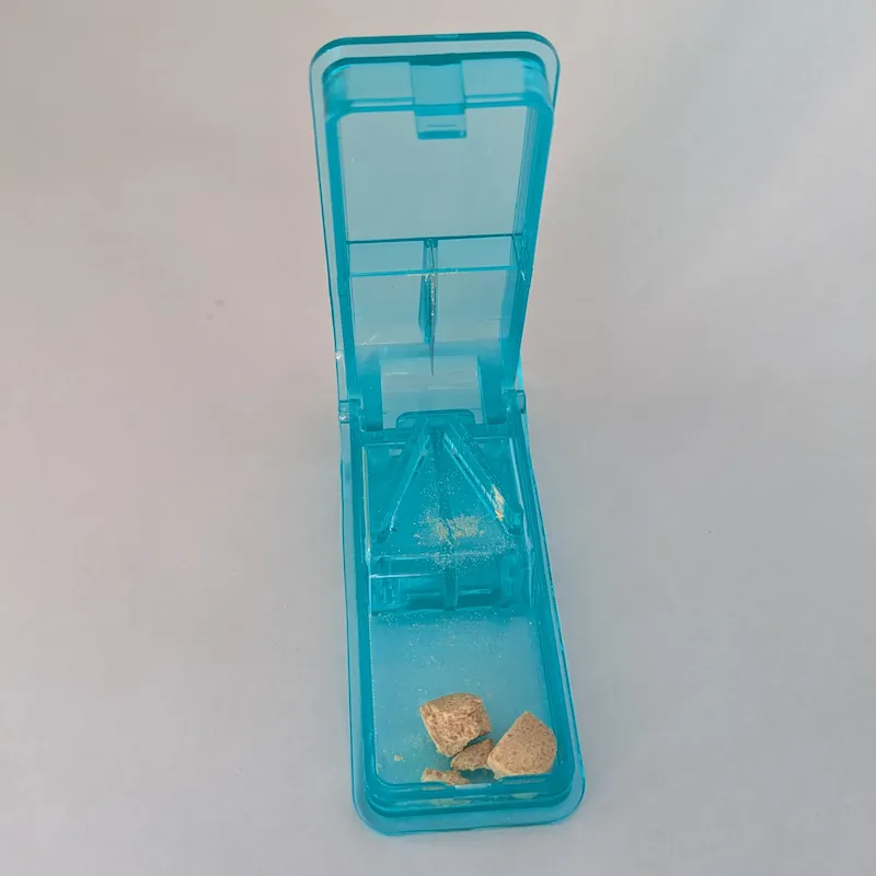 The blue pill splitter open, showing a tablet that has been cut into two halves.