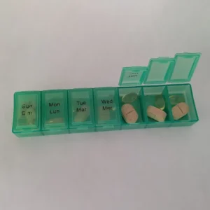 The green pillbox with several lids open, showing various pills and capsules organized by day.