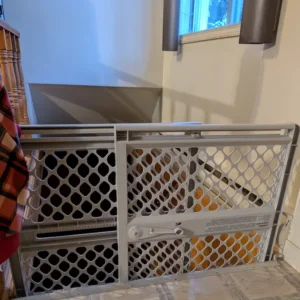 A grey pressure-mounted plastic safety gate installed at the top of indoor stairs.