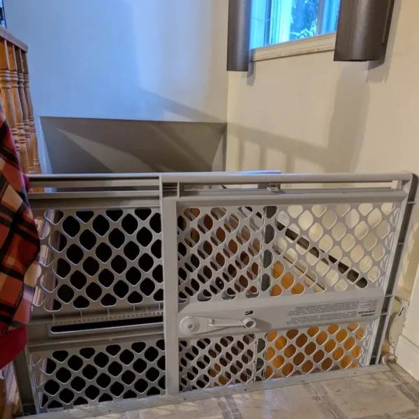 A grey pressure-mounted plastic safety gate installed at the top of indoor stairs.