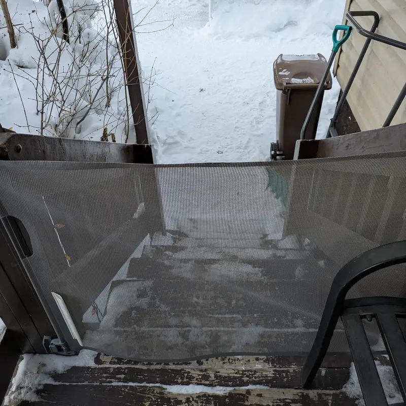 A retractable mesh screen gate installed on an outdoor deck overlooking snowy stairs.