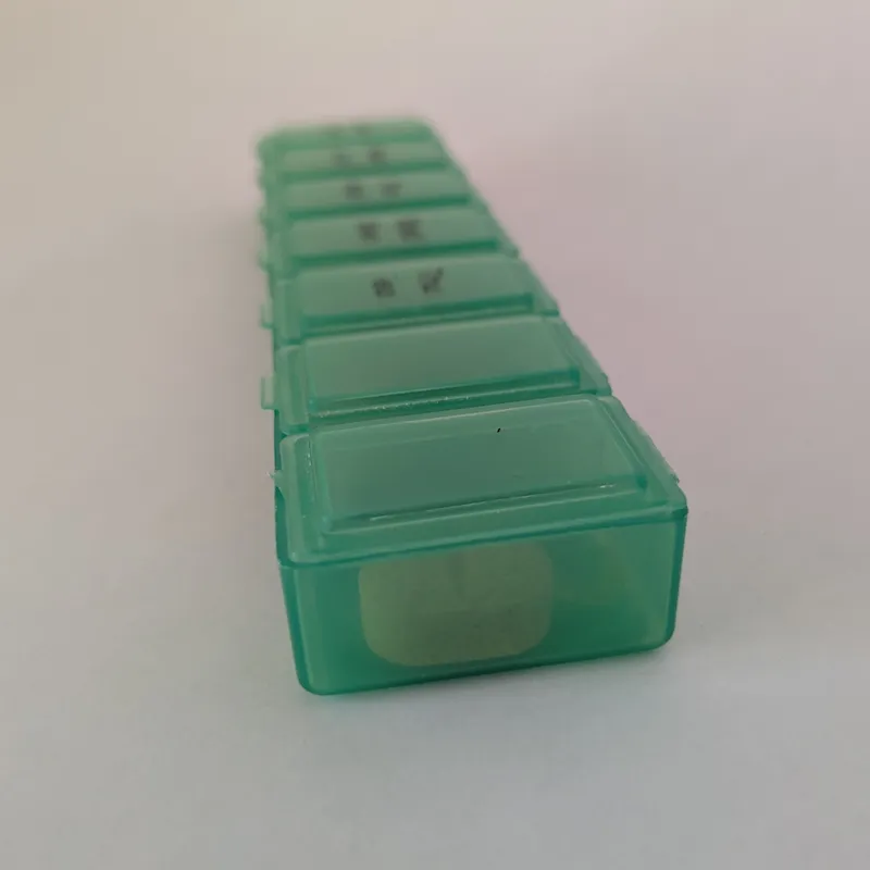 An angled close-up view of the green pillbox showing the Monday through Sunday markings on the lids.