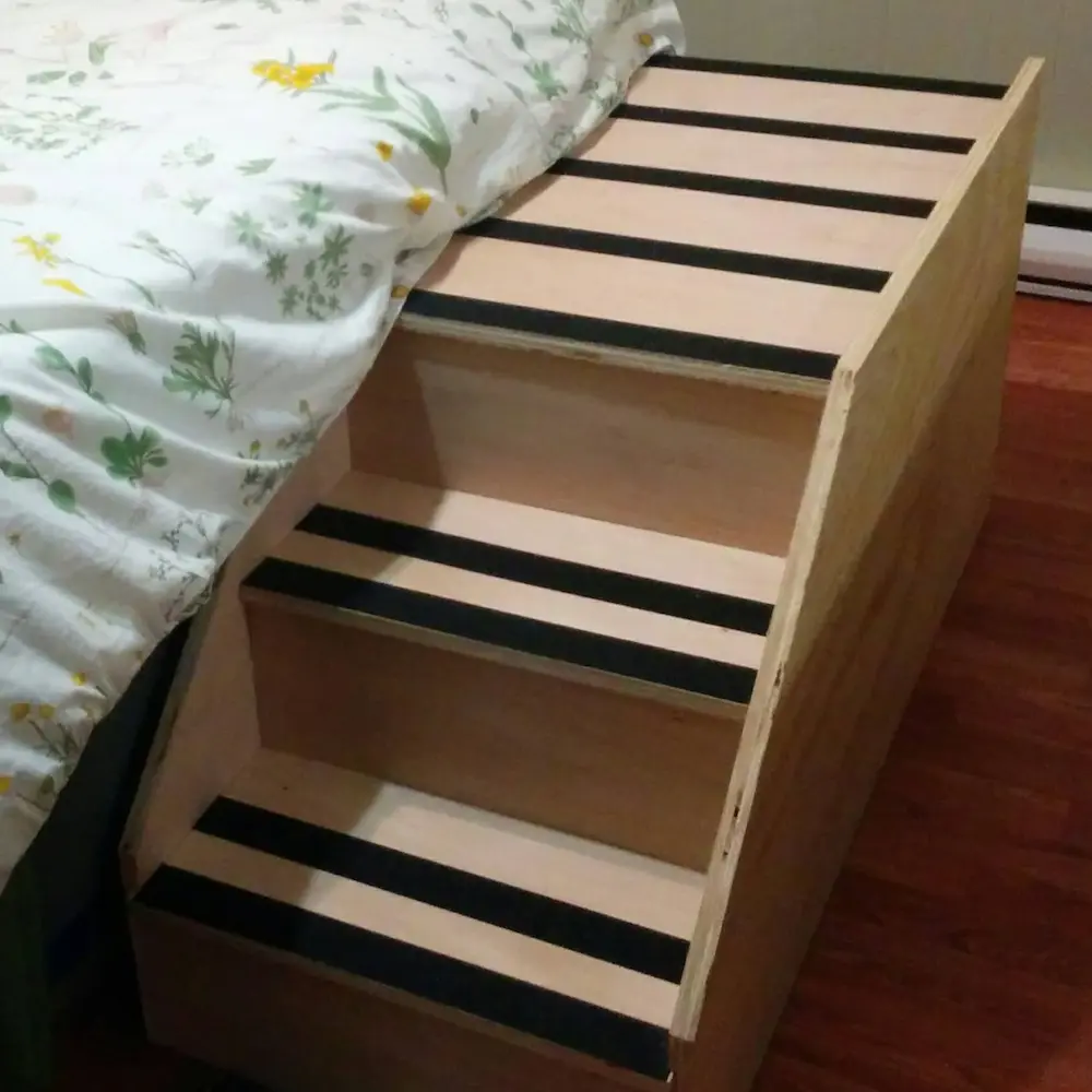 Custom-built wooden stairs with black non-slip grip tape, designed to help Maya get onto the bed.